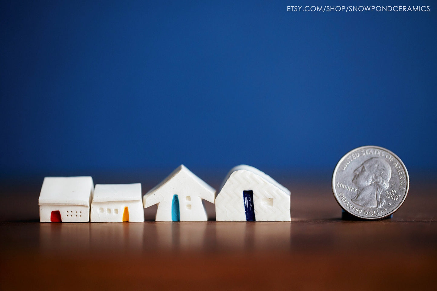 A set of four teeny tiny white cerami houses with red, yellow, and blue doors.