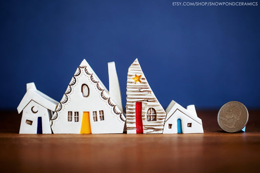 A miniature village of four ceramic houses that fit together like a puzzle. Some have storybook scalloped shingles and one has a tiny moon on the top.