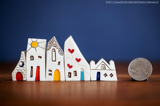 Five teeny tiny ceramic houses that together make a village. One has three trailing hearts, one has a sunshine on the roof.