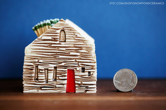 Ceramic house shaped match striker with log cabin wood texture and red door.